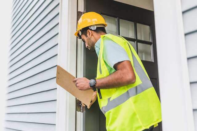person-in-ellow-safety-reflective-vest-with-hard-hat-doing-house-inspection